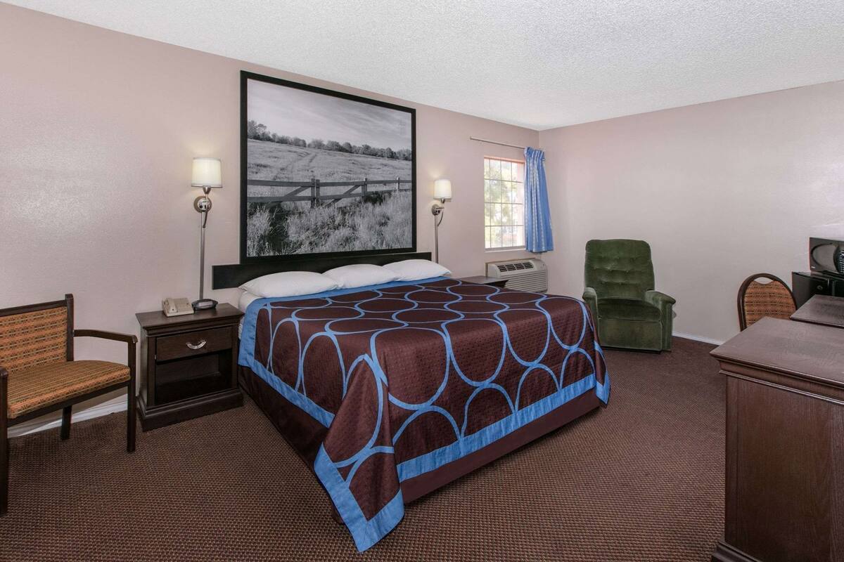 A hotel room with a bed, a desk, a chair, a television, and a window with curtains.