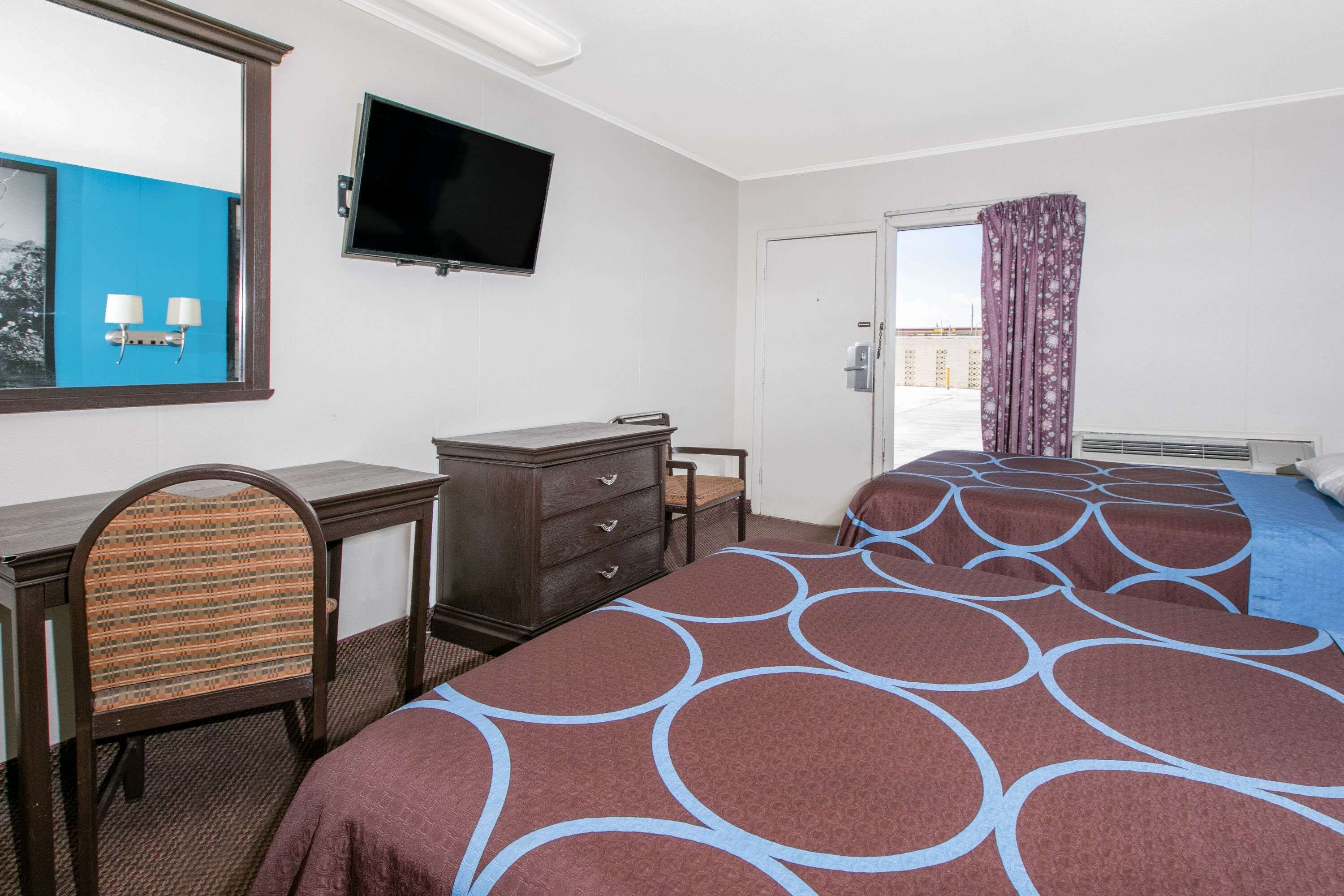 A hotel room with a bed, a desk, a chair, a dresser, a television, and a window with curtains.