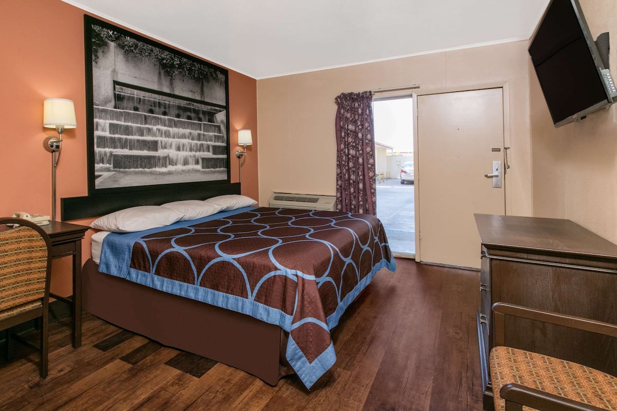 A hotel room with a bed, a desk, a chair, a TV, and a large window.