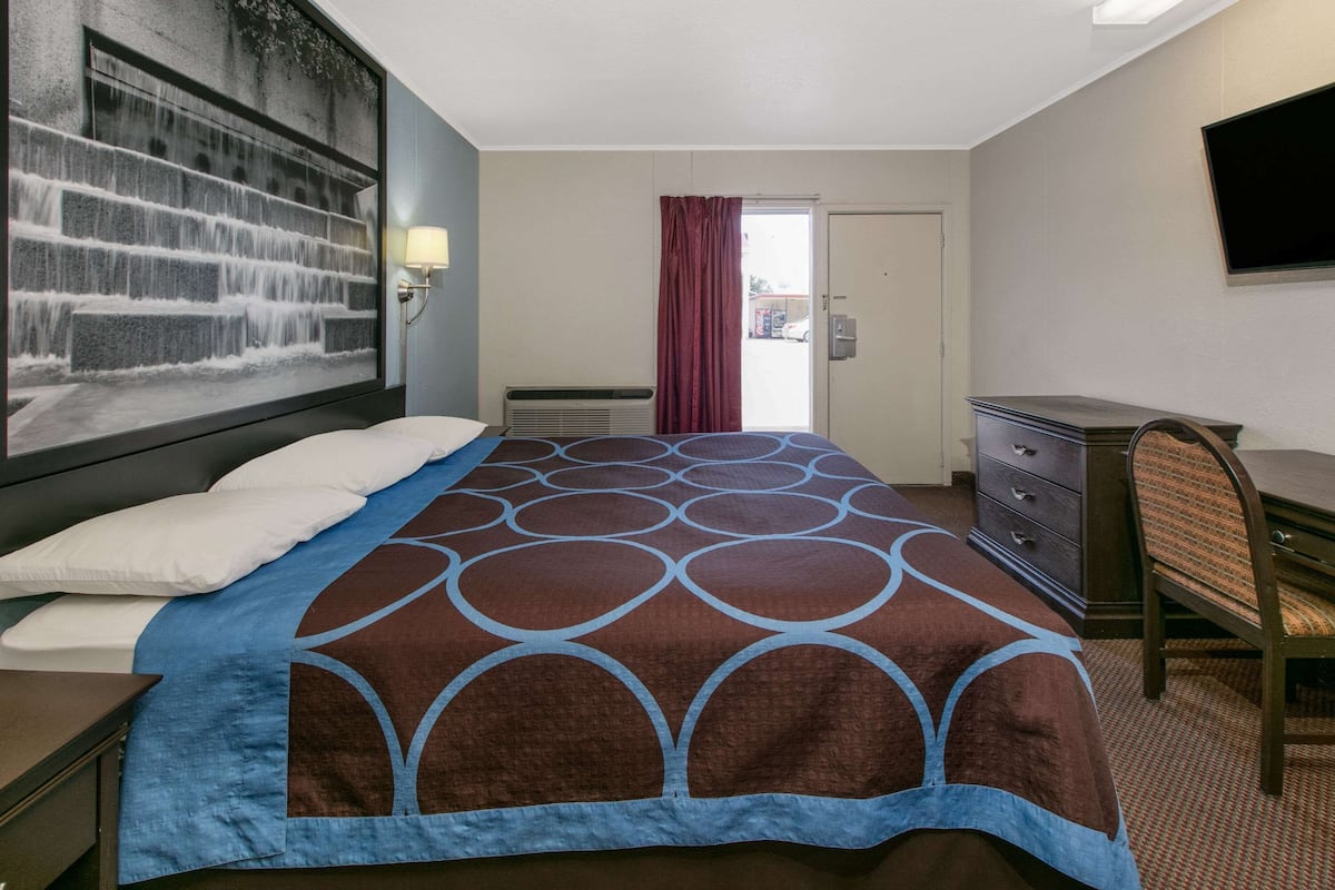 A hotel room with a bed, a desk, a chair, a television, and a large window with a view of the outside.
