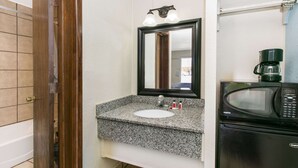 Un baño con lavamanos de granito, un espejo, cafetera y microondas.