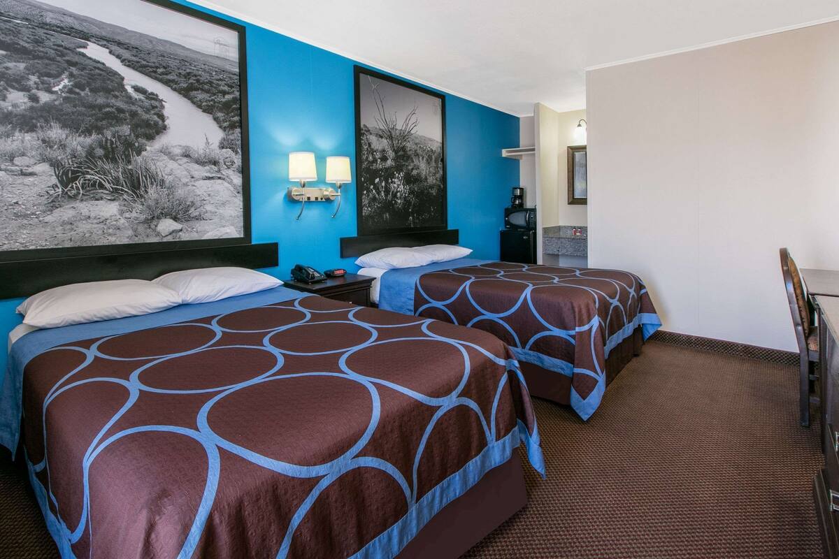 A hotel room with two beds, a desk, a chair, and a coffee machine.
