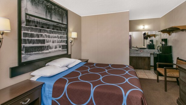 Habitación de hotel con cama, escritorio, silla, un cuadro grande, kitchenette y baño.