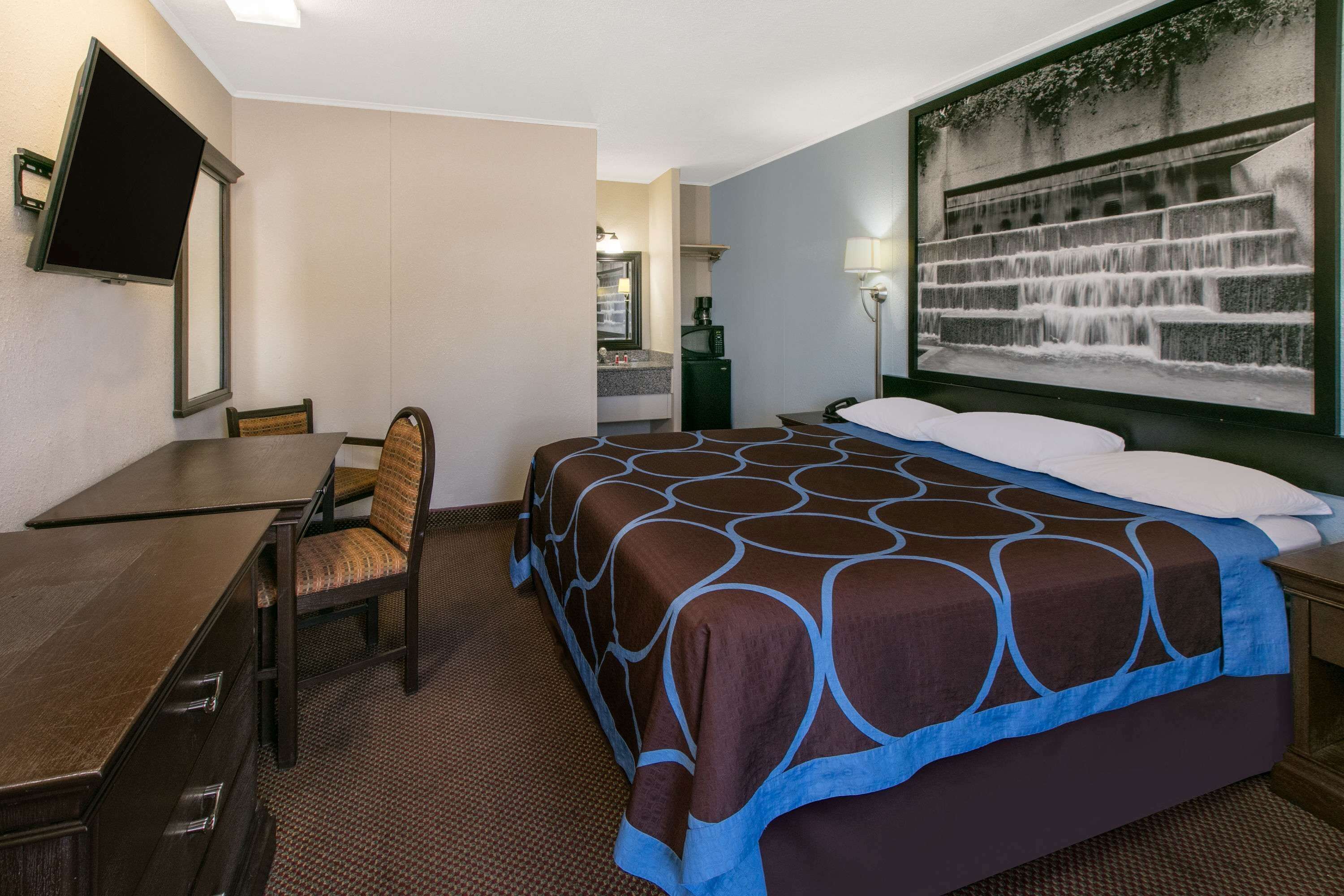 Une chambre d’hôtel comprenant un lit, un bureau, une chaise, une télévision, un tableau et une table de chevet.