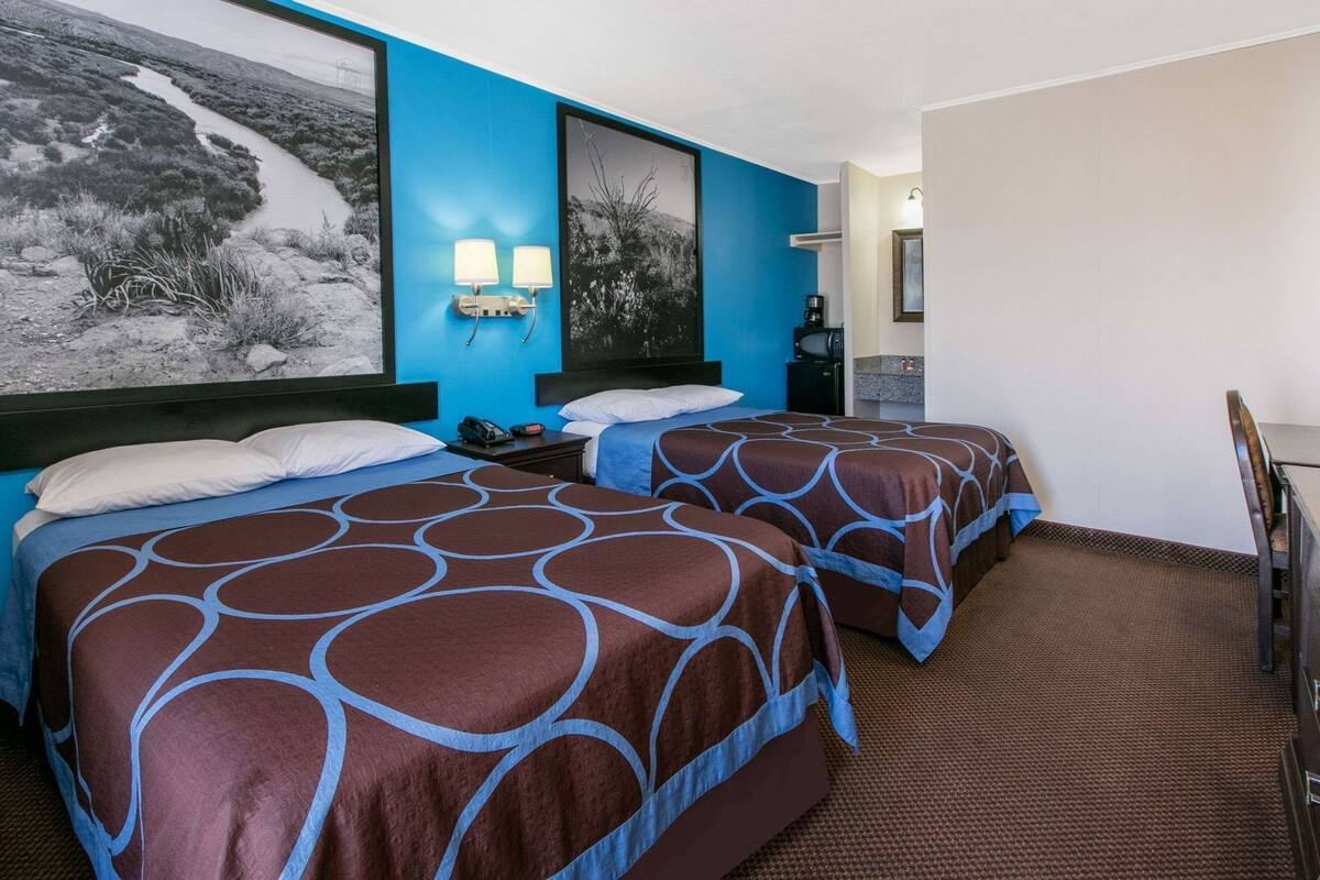 A hotel room with two beds, a large window with a view of a landscape, a wall-mounted light fixture, and a small table with a telephone.