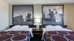 Een hotelkamer met twee bedden, een nachtkastje met een lamp, en twee grote zwart-witfoto’s aan de muur.