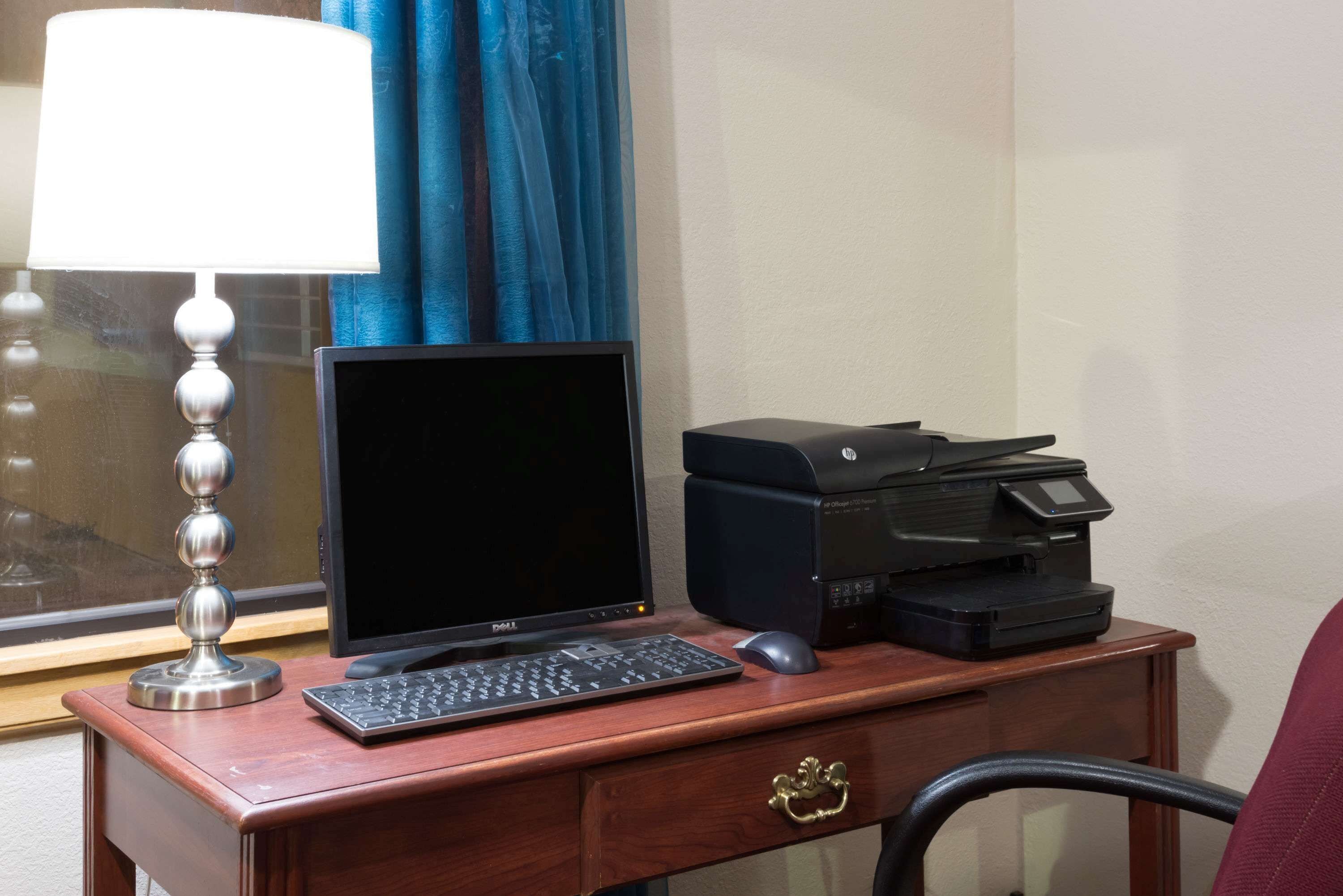 A wooden desk with a computer monitor, keyboard, mouse, and printer.