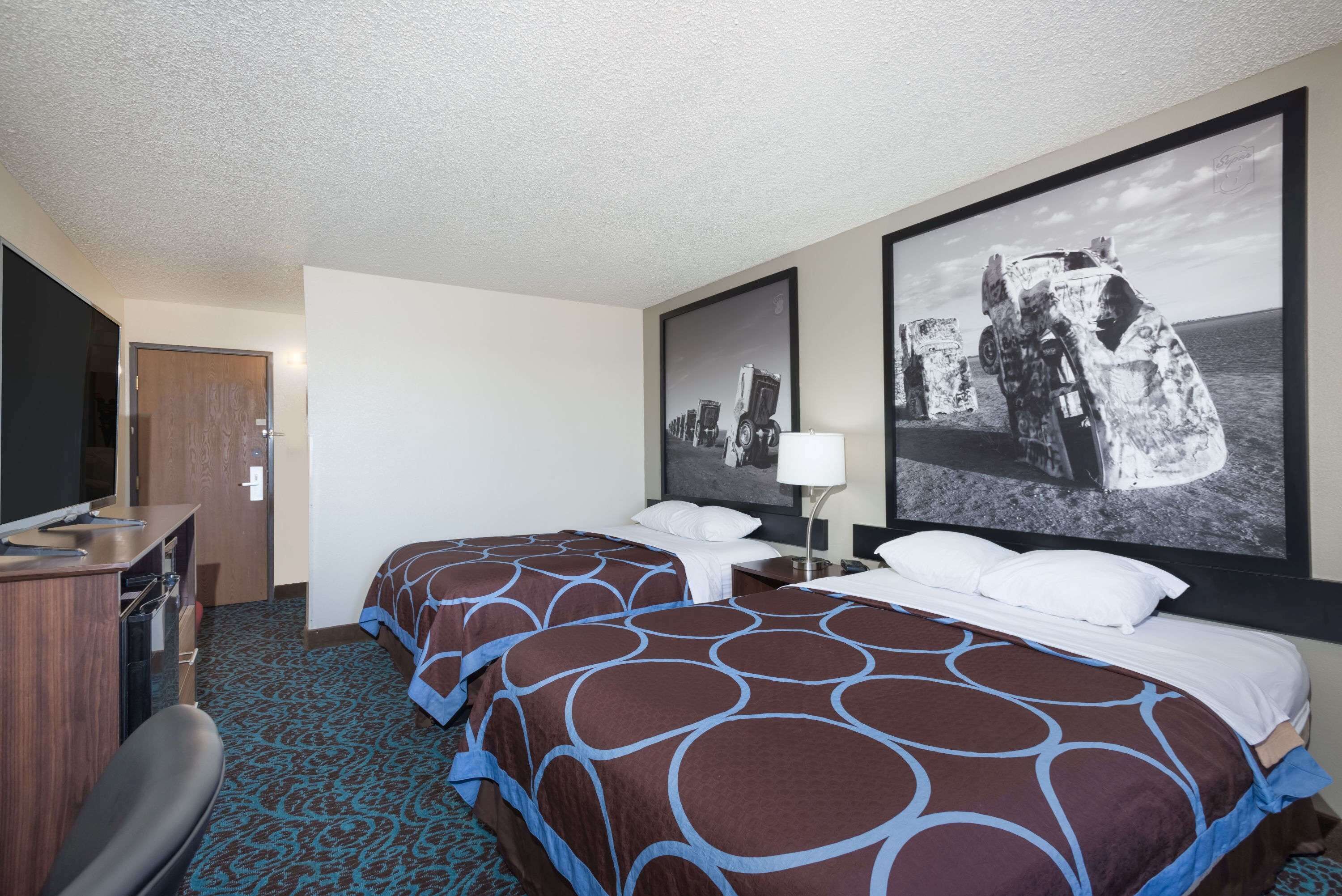 A hotel room with two beds, a desk, a chair, and a TV.