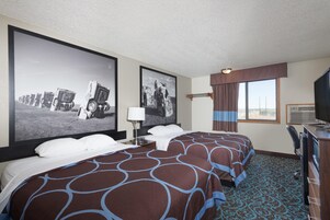 Una habitación de hotel con una cama grande, un escritorio con televisor y dos cuadros grandes en la pared.