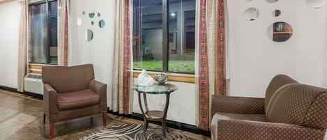 A room with two patterned armchairs, a glass table with a white sculpture, a patterned rug, and a large window with curtains.