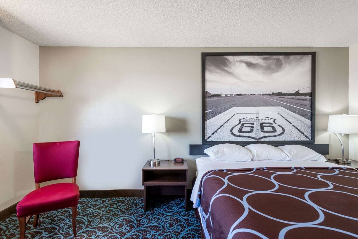 Ein Hotelzimmer mit einem Bett, einem roten Sessel, zwei Nachttischlampen, einem Nachttisch und einem großen Wandbild, das eine Straße zeigt.