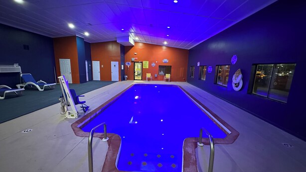 Een binnenzwembad met blauwe verlichting, een rolstoel en ligbedden.