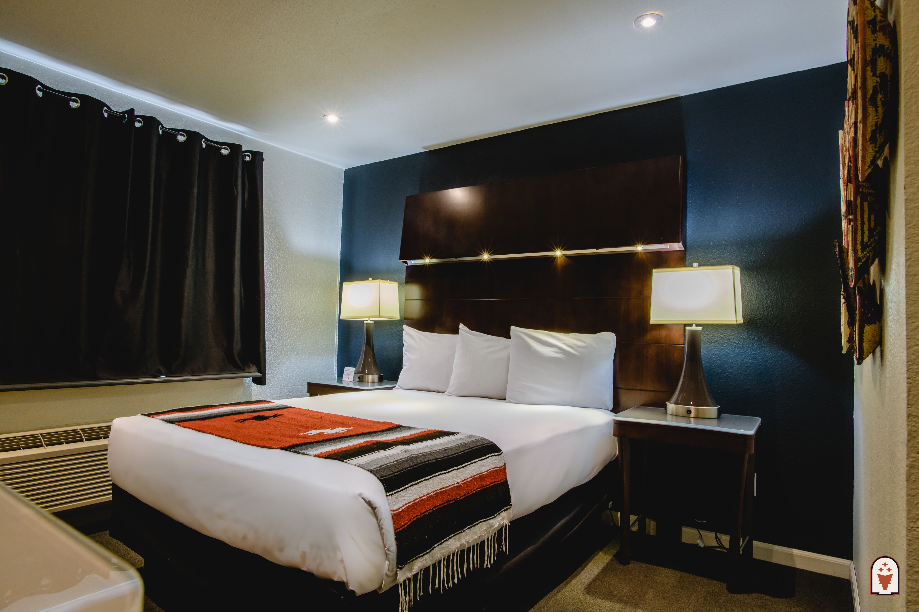 Ein Hotelzimmer mit einem großen Bett, zwei Nachttischen mit Lampen, einem Heizgerät und einem Fenster mit Vorhängen.