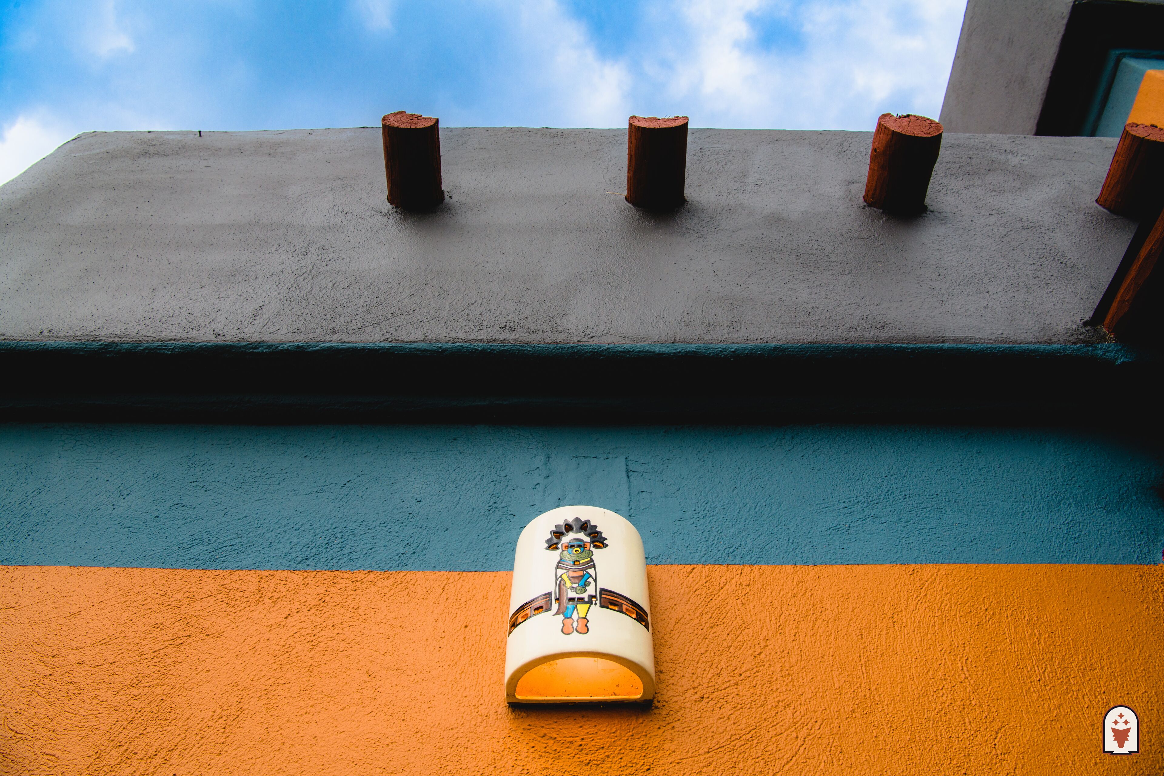 A white ceramic mug with a Native American design on a colorful wall.
