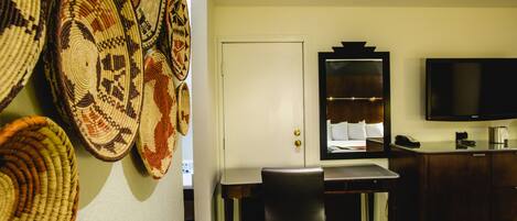 A hotel room with a bed, a desk with a chair, a television, and a wall adorned with woven baskets.