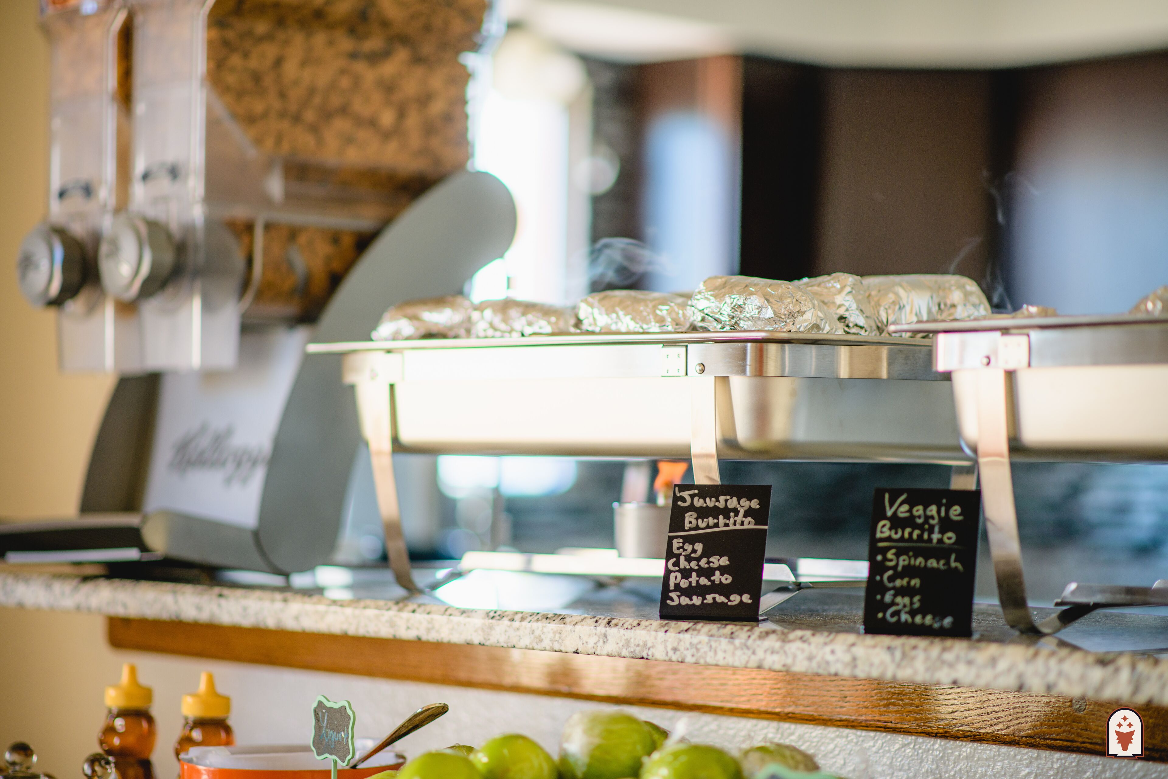 A kitchen counter with a coffee machine and a menu board listing options for sausage and veggie burritos.