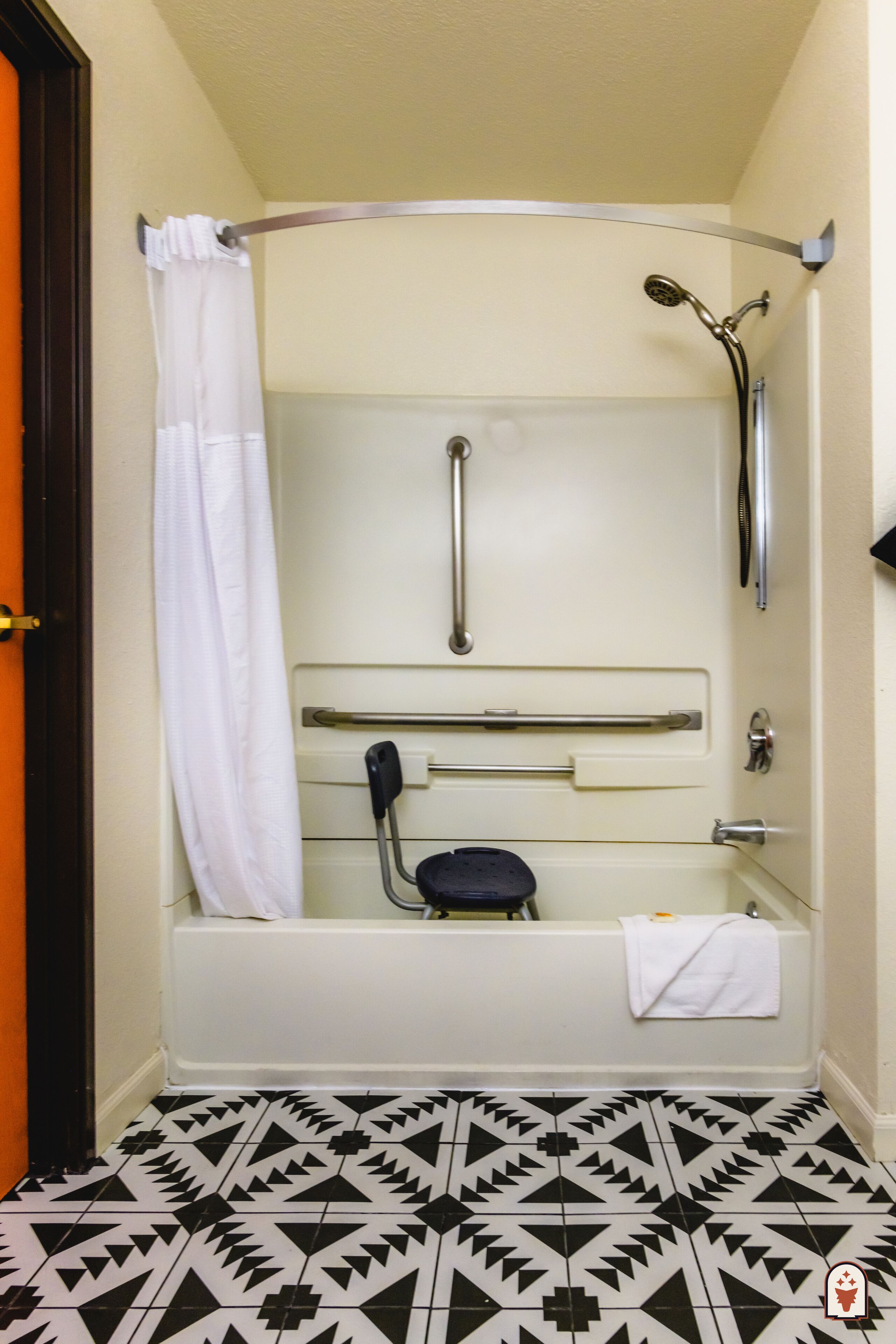 A bathroom with a shower, grab bars, a white bathtub, and a patterned floor.