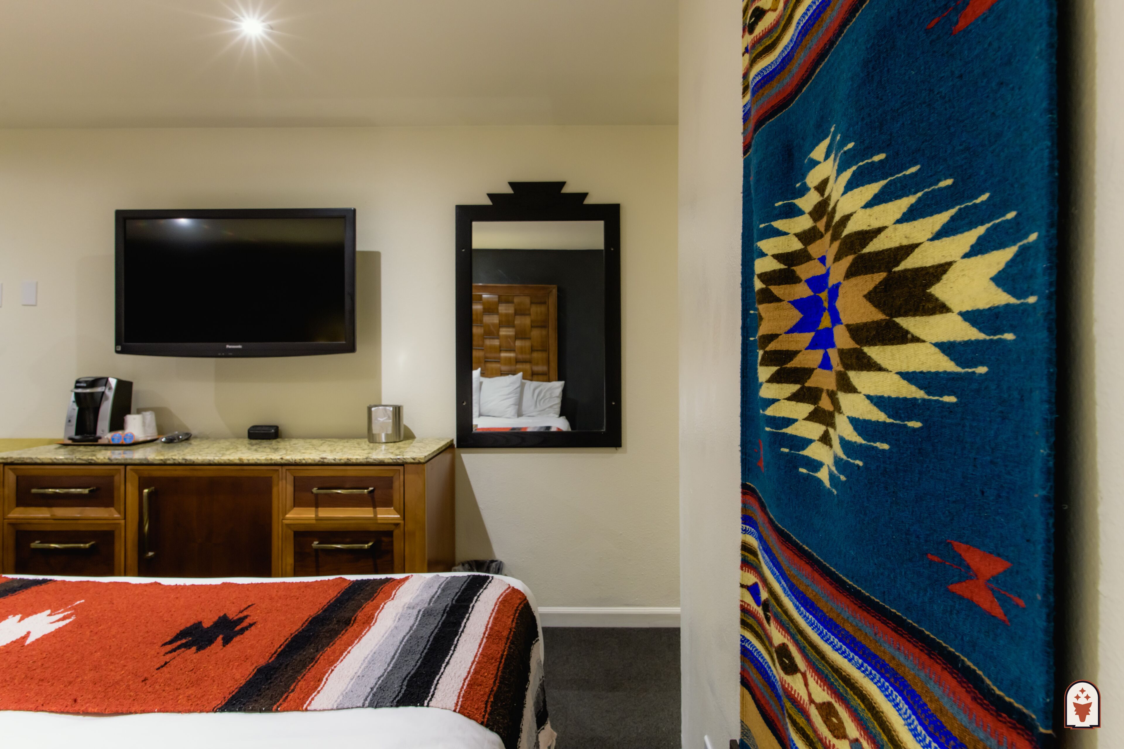 Ein Hotelzimmer mit Bett, Wandfernseher, Holzkommode und Spiegel.