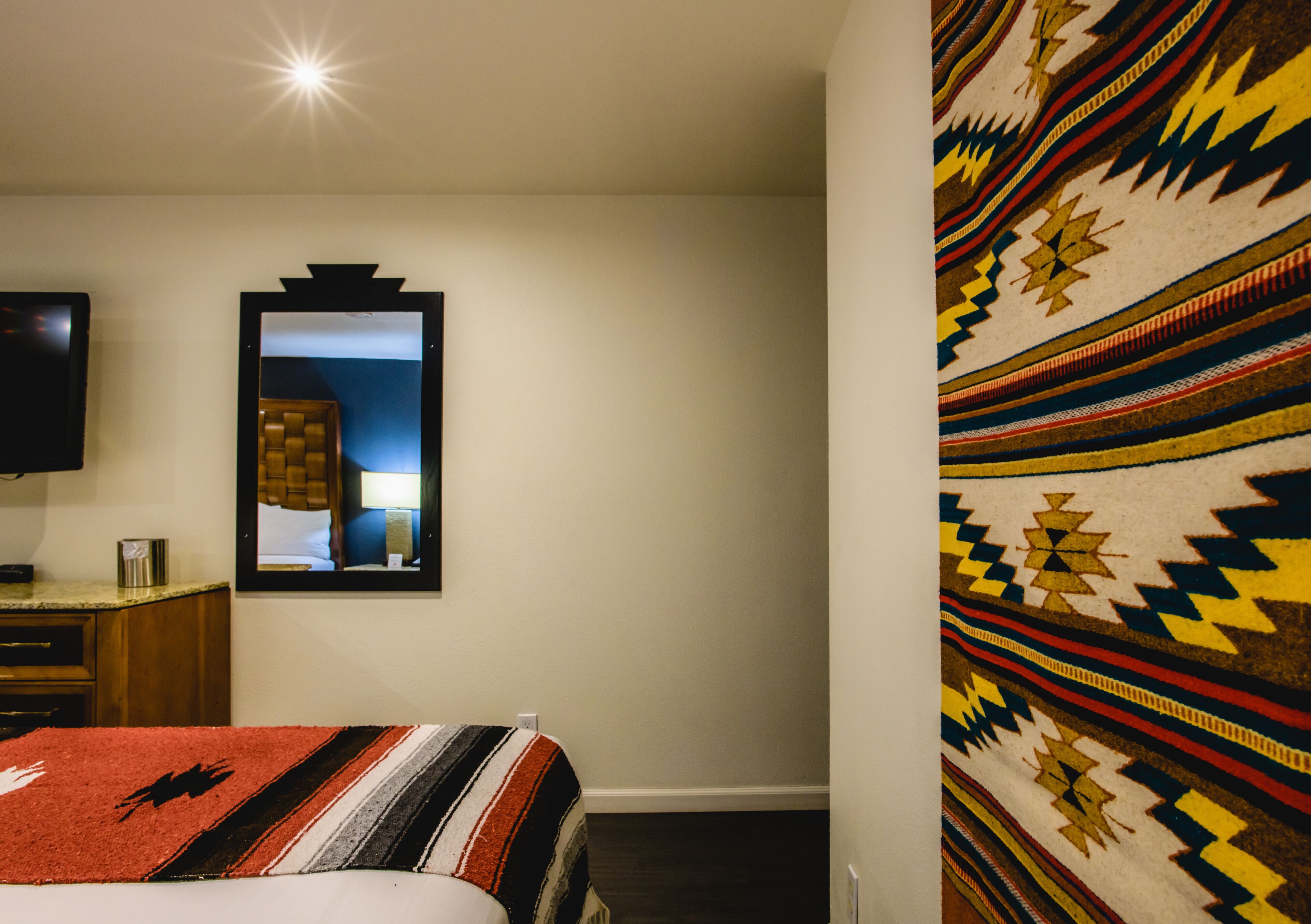 Hotellihuone, jossa on sänky, televisio, peili ja kuviollinen seinä.