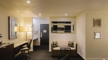 A hotel room with a desk, chair, sofa, and a small table. There are two mirrors on the walls and a door leading to another room.