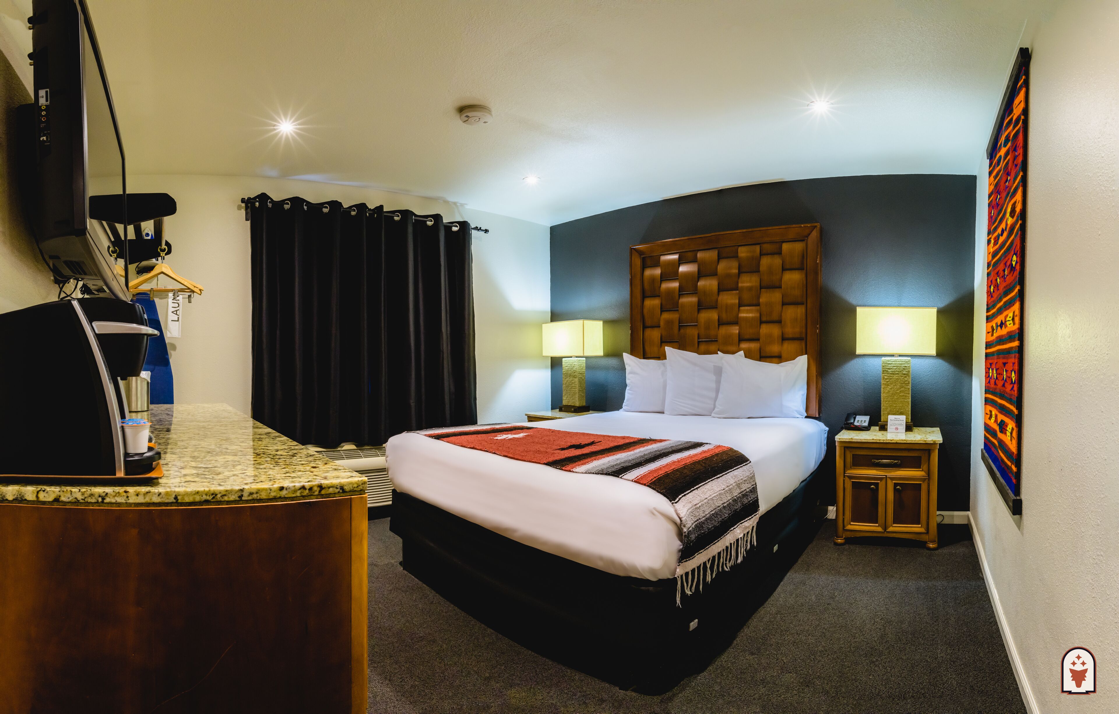 A hotel room with a bed, a desk with a coffee maker, two bedside lamps, and a small cabinet.