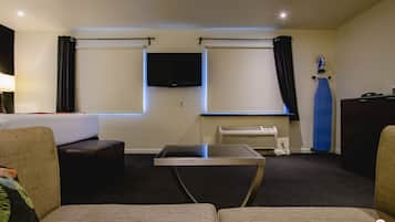 A hotel room with a sofa, a small table, a flat-screen TV mounted on the wall, and a window with curtains.