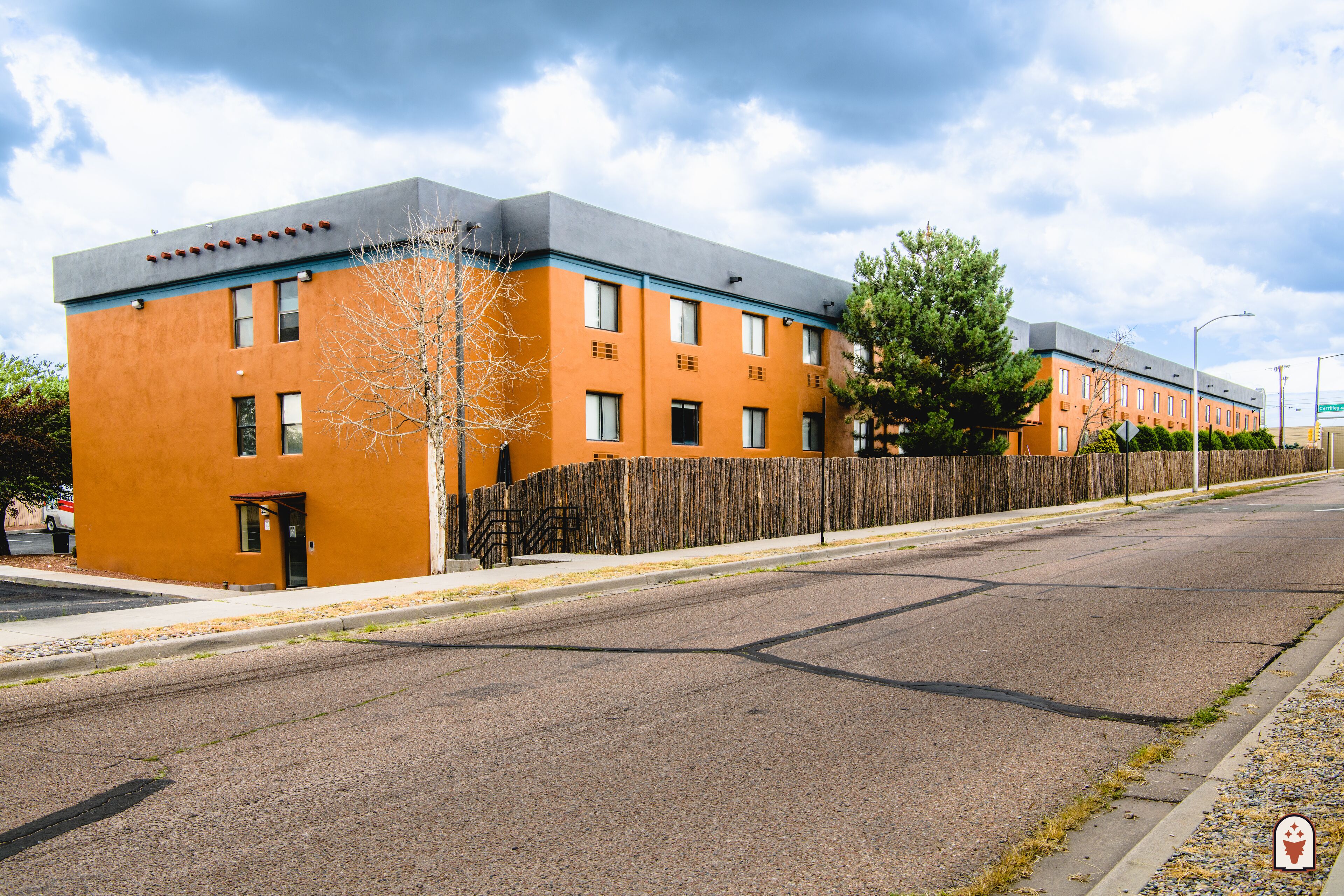 A multi-story building with a flat roof, a wooden fence, and a clear sky.
