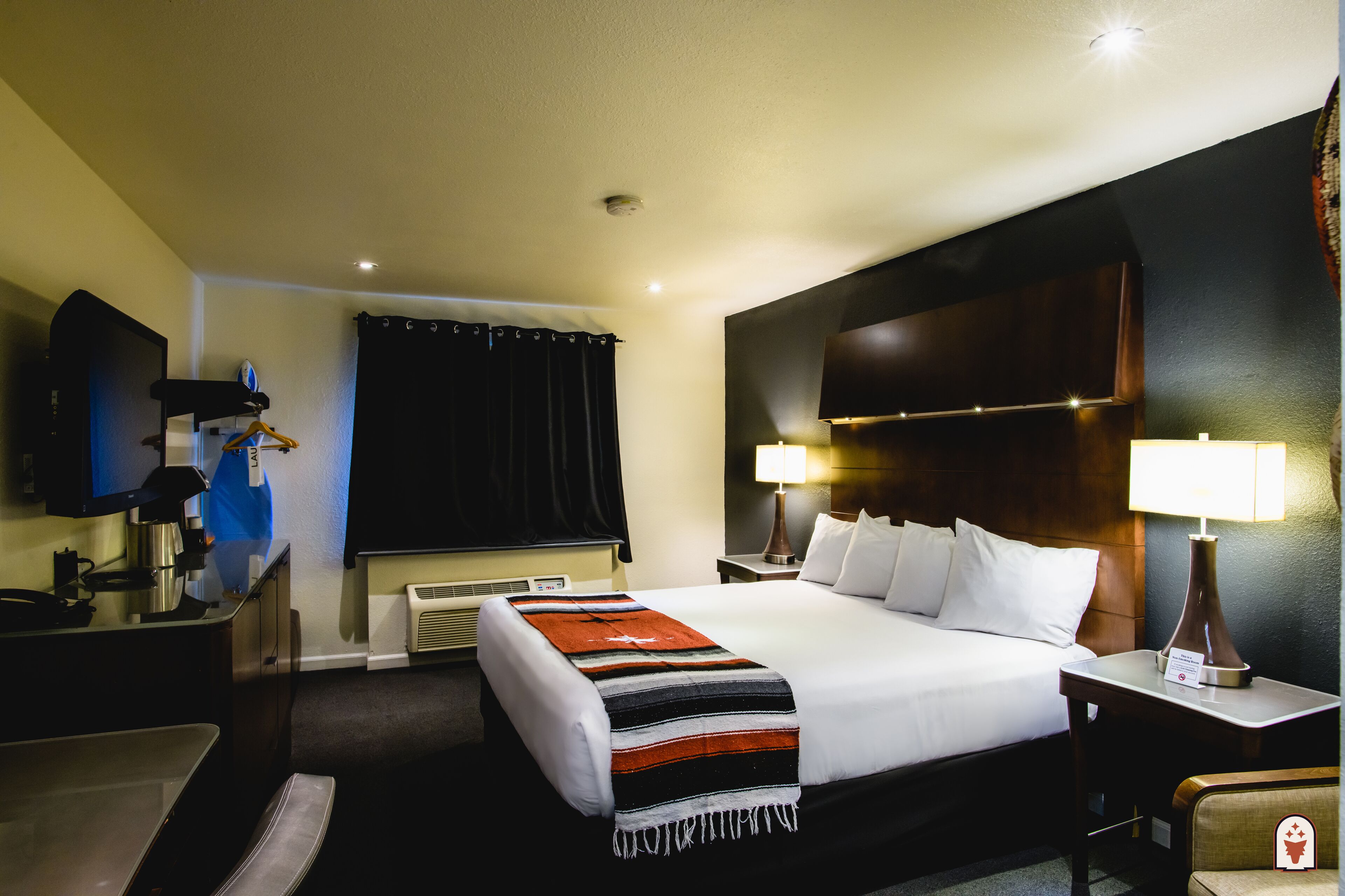 Una habitación de hotel con una cama grande, un escritorio con lámpara, un televisor y un perchero.