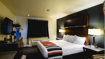 Una habitación de hotel con una cama grande, un escritorio con lámpara, un televisor y un perchero.