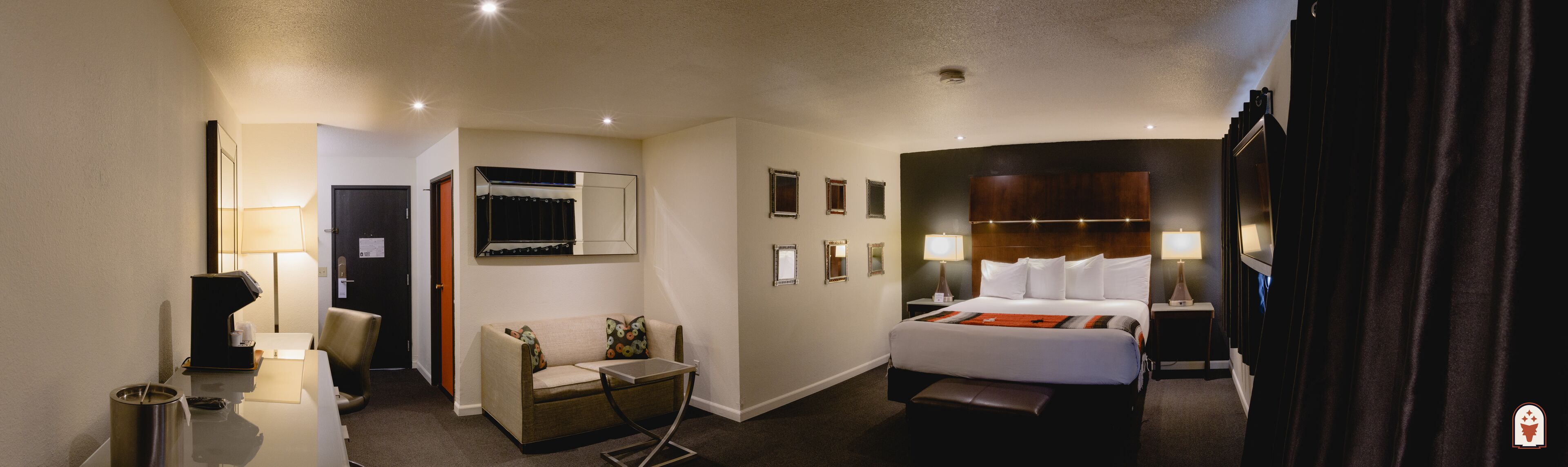 A hotel room with a bed, bedside table, lamp, chair, and a desk with a lamp.