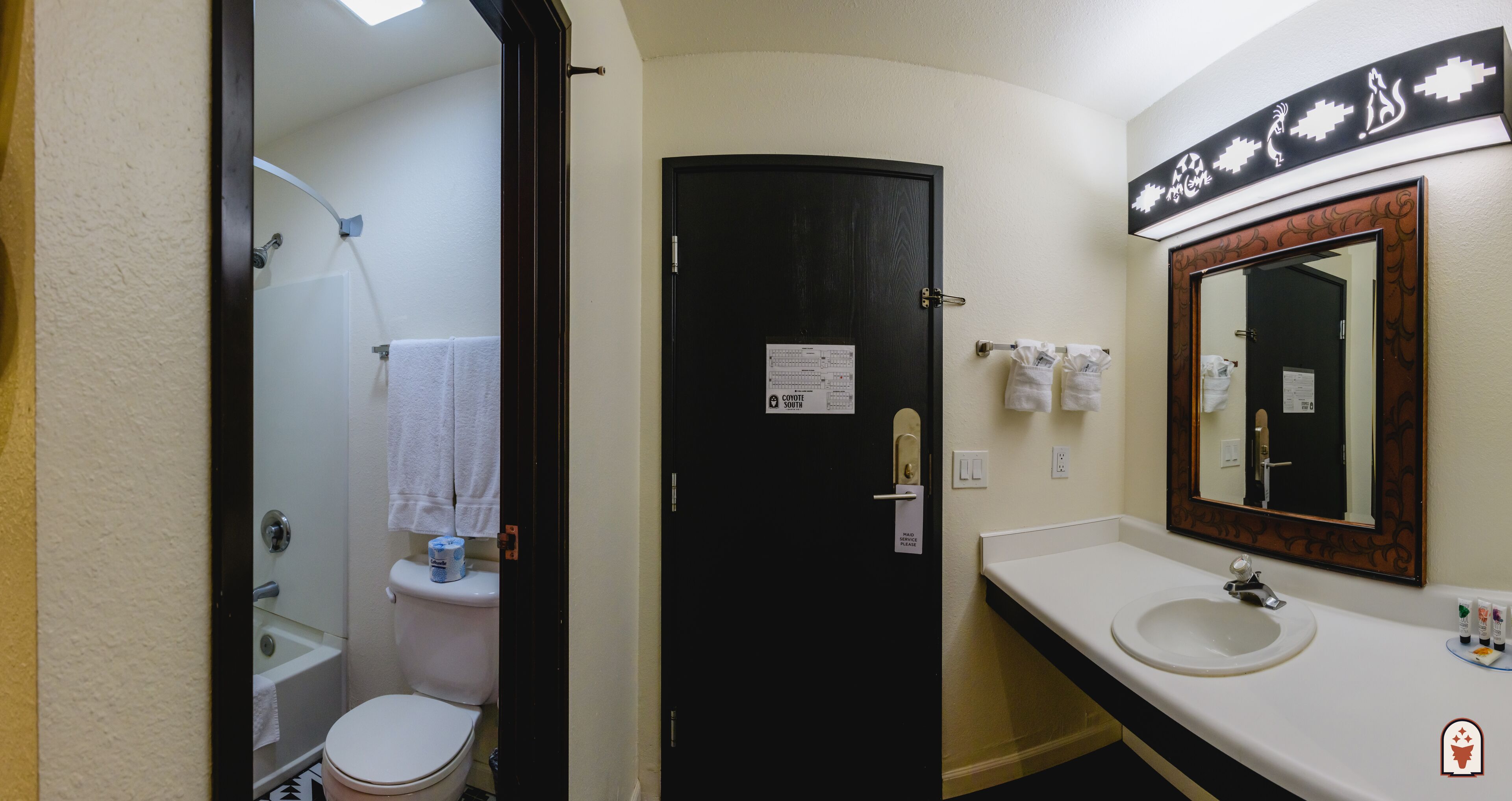 A bathroom with a toilet, sink, and mirror. There is a door with a sign on it, and towels hanging on the wall.