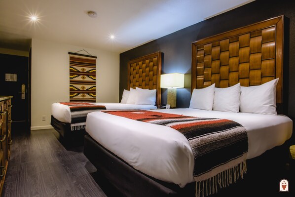 A hotel room with two beds, a wooden headboard, a wall-mounted lamp, and a patterned wall hanging. - Coyote South (Santa Fe)