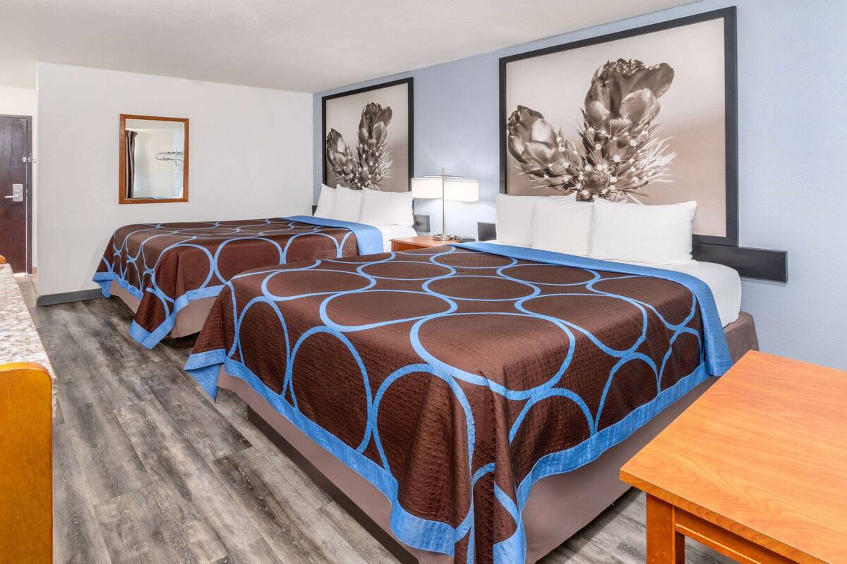 Une chambre d’hôtel avec deux lits, une table en bois et des œuvres d’art accrochées aux murs.