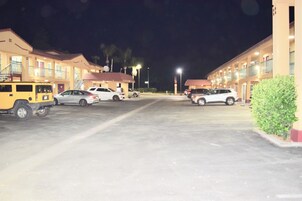 Un estacionamiento de hotel con varios coches aparcados, una camioneta SUV amarilla y un edificio con balcones y una escalera.