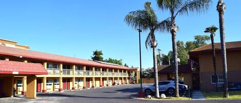Un motel con techo rojo y varios balcones, un estacionamiento y palmeras.