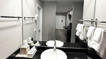 A hotel bathroom with a black sink, a large mirror, and a towel rack with white towels.