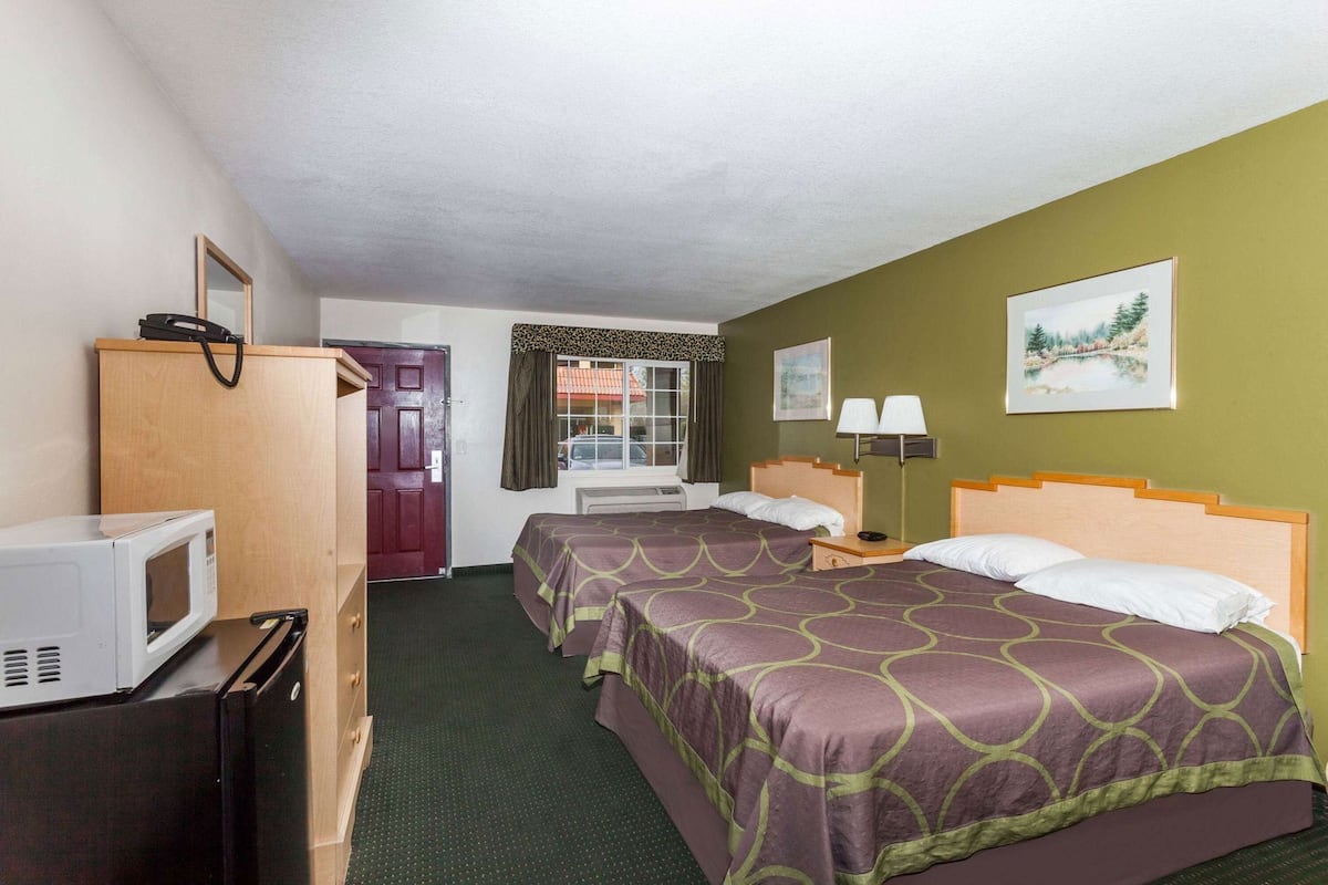 Ein Hotelzimmer mit zwei Betten, einer Mikrowelle, einem Schreibtisch, einem Stuhl, einem Kleiderschrank und einem Fenster mit Vorhängen.