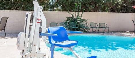 A pool area with a diving board, blue lounge chairs, and a concrete wall.