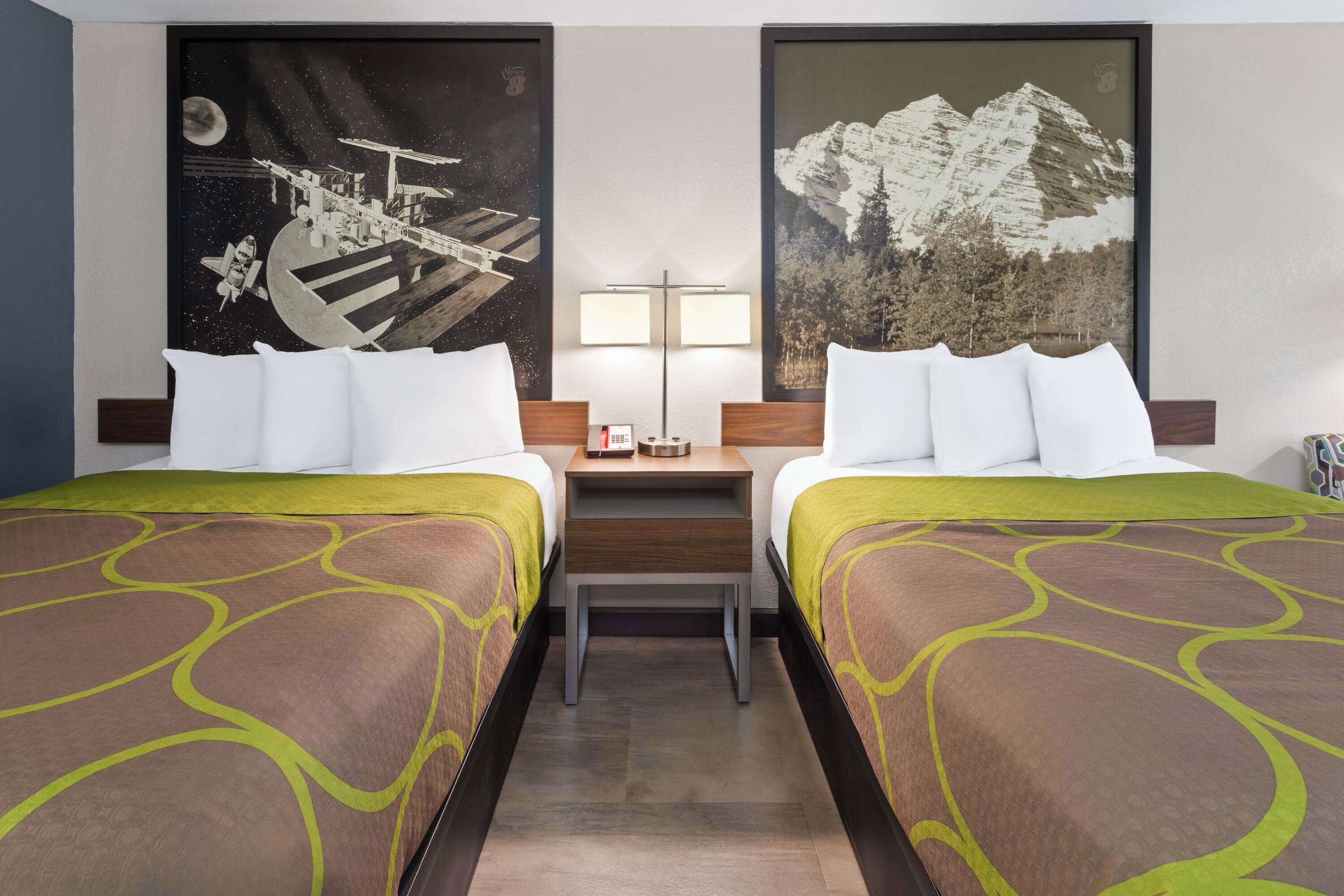 Une chambre d’hôtel avec deux lits, une table de chevet, une lampe et deux grandes œuvres d’art mural représentant l’espace et des montagnes.