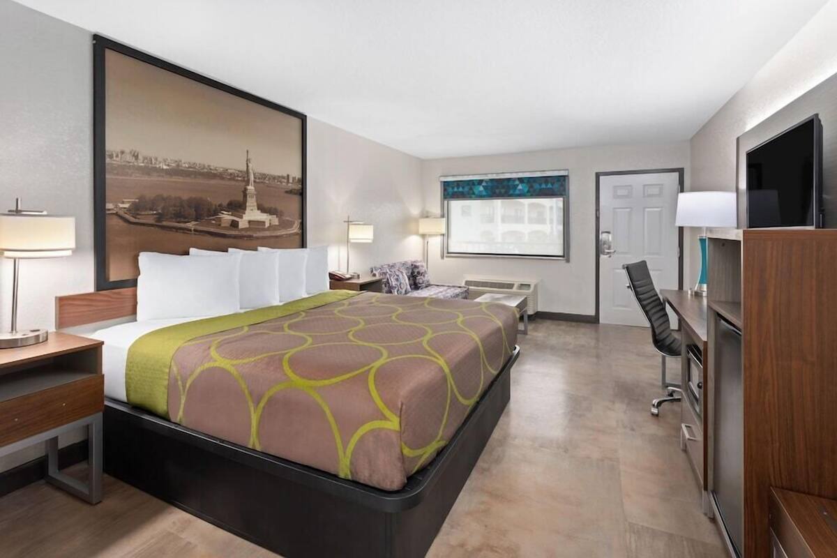 A hotel room with a bed, desk, chair, TV, and artwork on the walls.