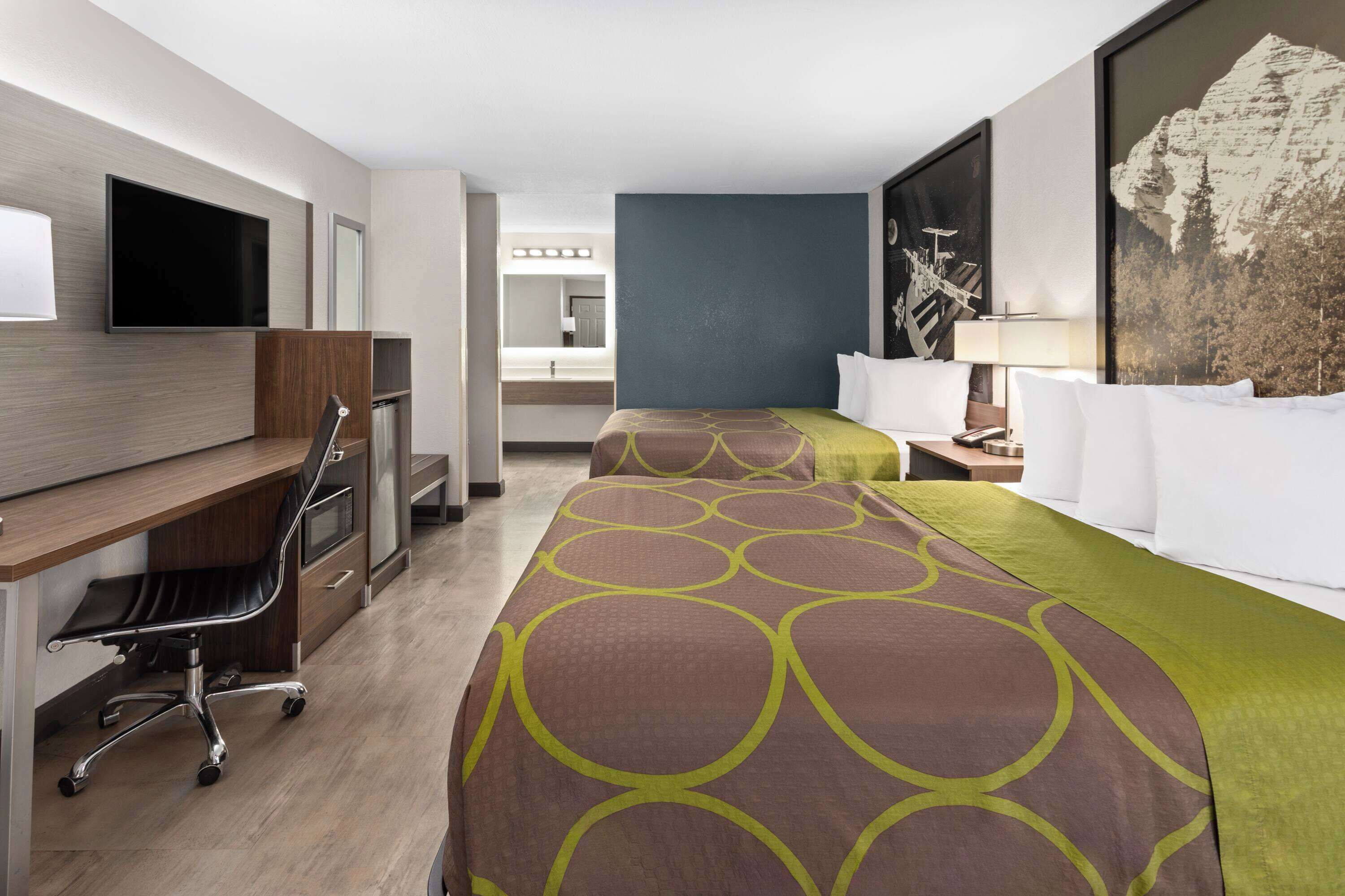 Ett hotellrum med två sängar, ett skrivbord, en stol, en tv och en stor tavla på väggen.
