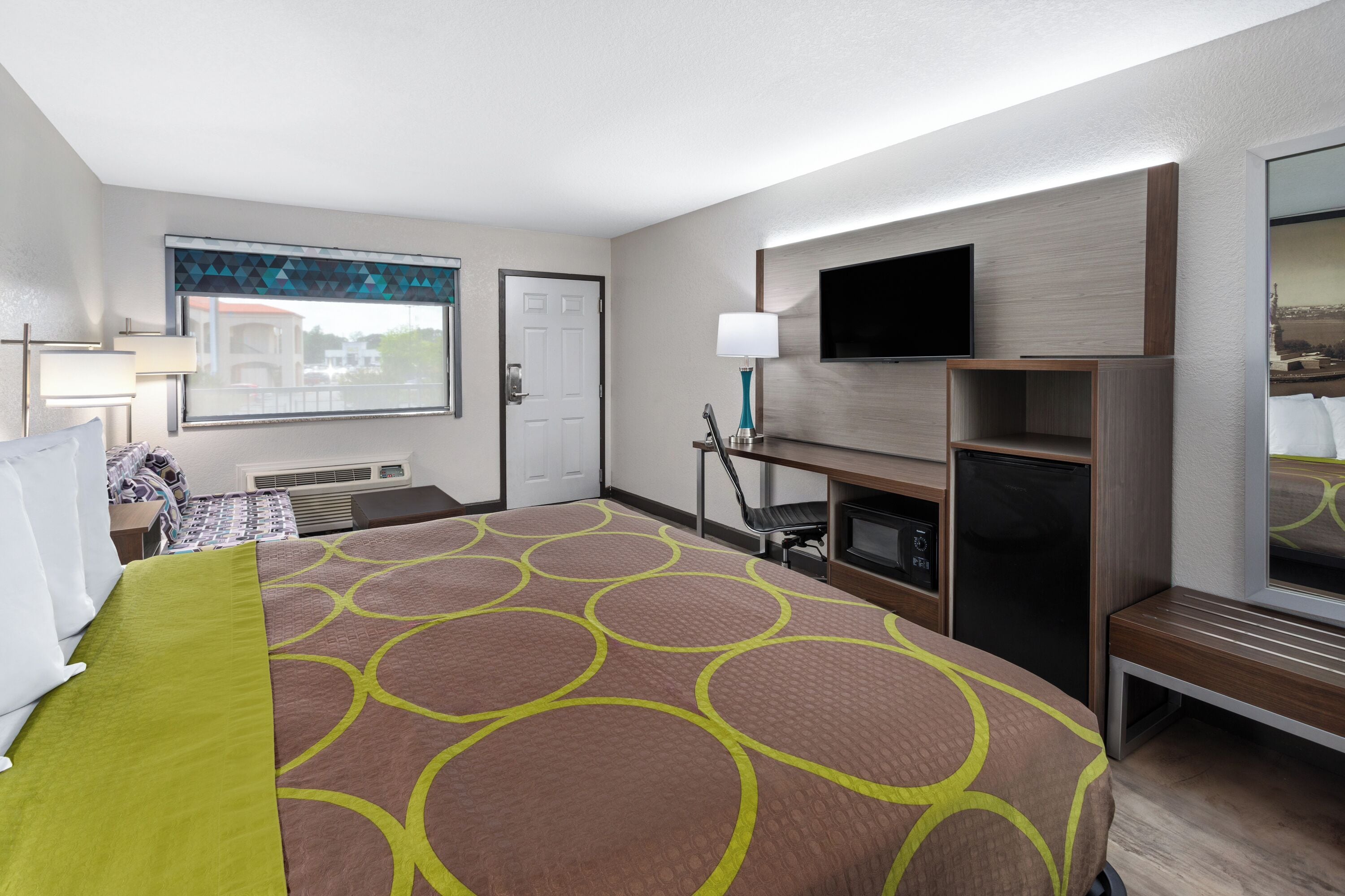 Hotelkamer met een groot bed, een flatscreen televisie aan de muur, een bureau met stoel en een raam met uitzicht op gebouwen.