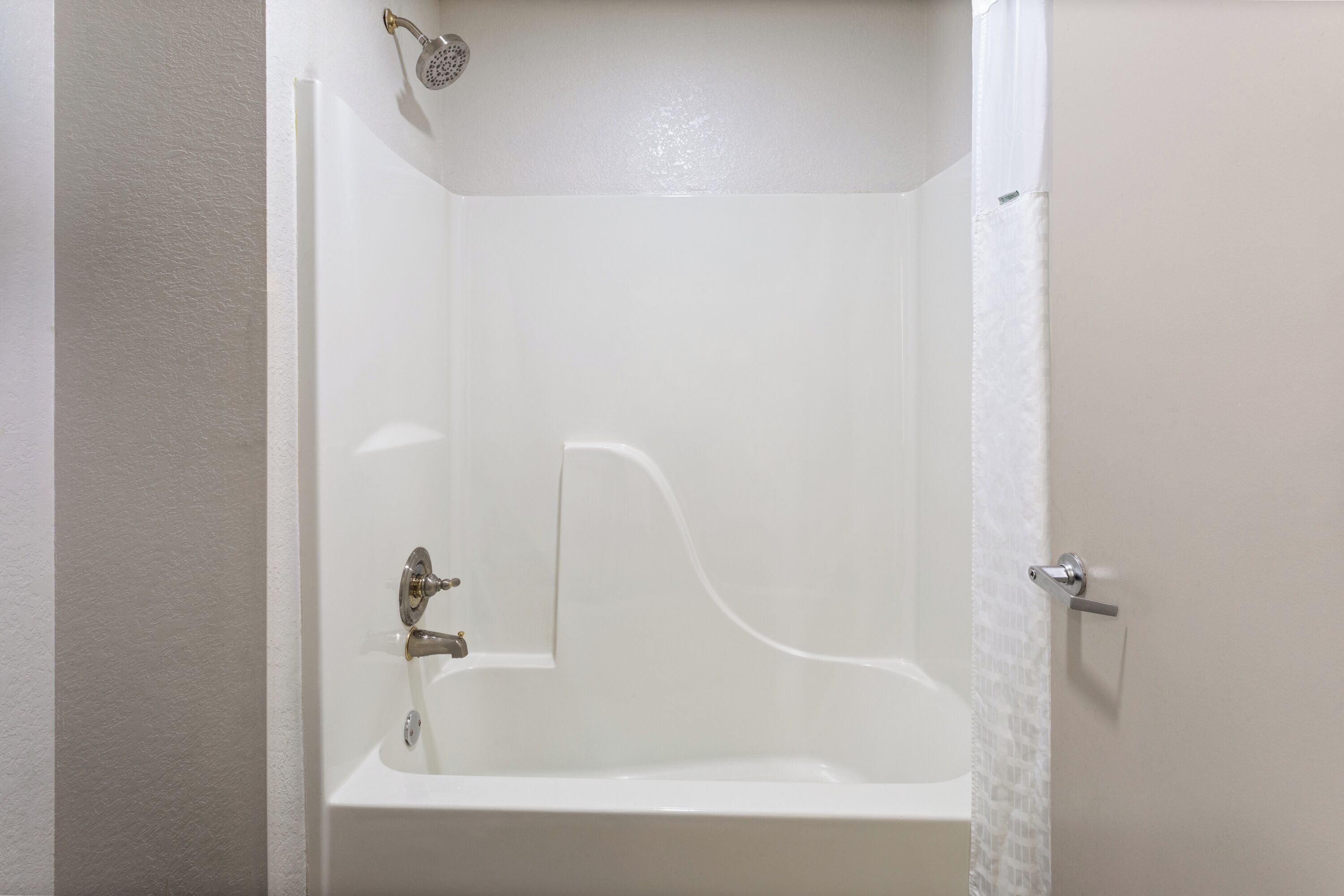 A white bathtub with a showerhead, a faucet, and a door handle.