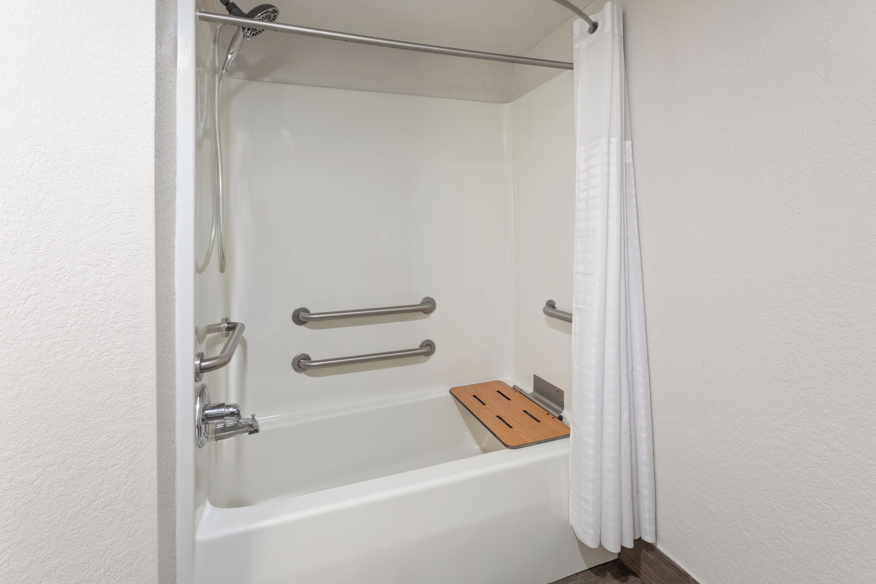 A white bathtub with a wooden tray, metal grab bars, and a showerhead.