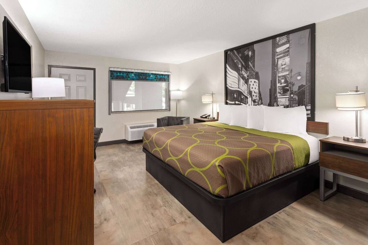 A hotel room with a large bed, a desk, a chair, a TV, a window, and a door.
