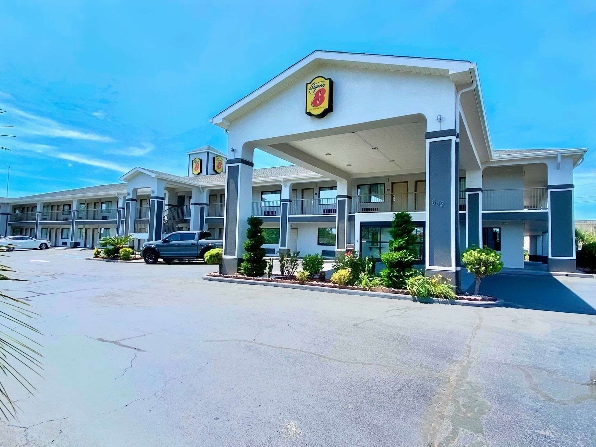 Un motel con entrada central, varios balcones y un estacionamiento.