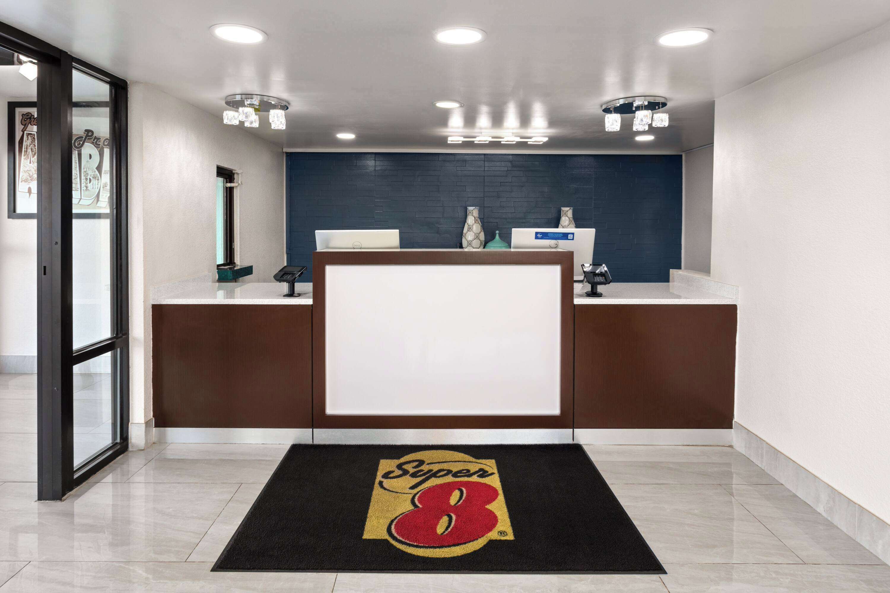 Un espace d’accueil comprenant un comptoir de réception, un paillasson noir orné d’un logo et un mur bleu agrémenté d’un vase décoratif.