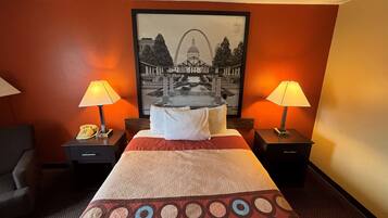 A hotel room with a large bed, two bedside tables with lamps, a telephone, and a framed picture of a bridge and fountain on the wall.