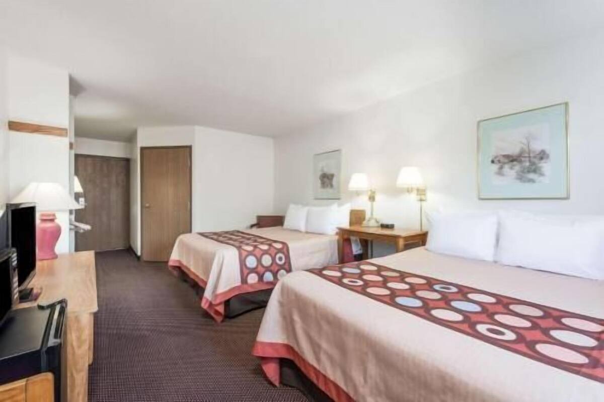 A hotel room with two beds, a desk, a chair, a television, and a door.