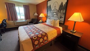 Una habitación de hotel con una cama, dos lámparas de noche, una silla, un escritorio y un ventanal con cortinas.